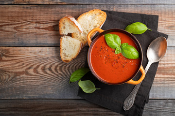 Homemade tomato soup with Basil, toast and olive oil on a wooden table. Prepared a vegetarian dish on a dark background. Top view with copy space