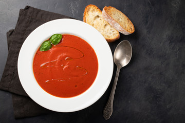 Homemade tomato soup with Basil, toast and olive oil on the stone table. Prepared a vegetarian dish on a dark background. Top view with copy space