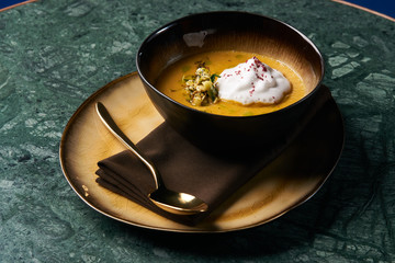 Hot Pumpkin cream soup with cream and pumpkin seeds, coconut milk, green oil, sprouts of lentils in bowl plate on table, top view, close-up. Delicious vegetarian diet food 