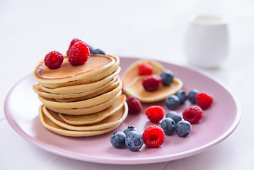 Homemade delicious pancakes with fresh berries in a violet plate on a white background. A tasty and healthy breakfast of pancakes with raspberries, blueberries and fresh milk.