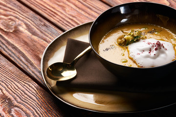 Hot Pumpkin cream soup with cream and pumpkin seeds, coconut milk, green oil, sprouts of lentils in bowl plate on table, top view, close-up. Delicious vegetarian diet food 
