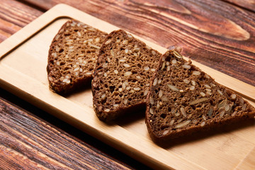 Slices of black rye bread. Three slices of fresh triangular rye bread with seeds on cutting board on rustic wooden table, top view, close-up