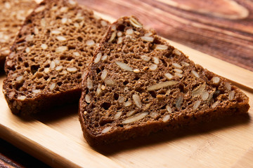 Slices of black rye bread. Three slices of fresh triangular rye bread with seeds on cutting board on rustic wooden table, top view, close-up