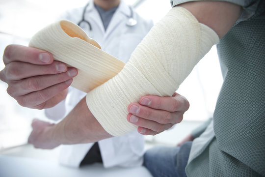 Orthopedist applying bandage onto patient's hand in clinic