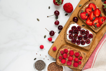 Healthy breakfast toasts with peanut butter, soft cheese, cherries, strawberries, raspberries, chia and flax seeds
