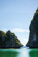 Two yellow kayaks in the distance on Halong bay between karst rock formations.