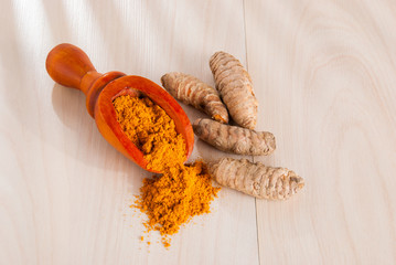 Turmeric powder and fresh turmeric on wooden background