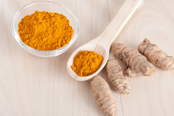 Turmeric powder and fresh turmeric on wooden background