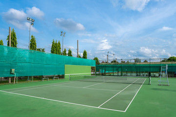 Empty Hard tennis court and net outdoor with blue sky clouds on a sunny day. 
Modern lifestyle with sport and fitness details