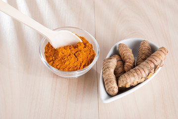 Turmeric powder and fresh turmeric on wooden background