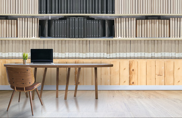 Modern office interior with laptop on wooden table and shelves of documents folder