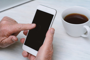 Top view of old man hand holding a cup of coffee and smartphone