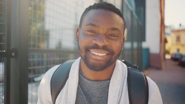 Handsome optimistic African student with beautiful smile looking directly at camera, smiling. Portrait of attractive young man on background of street. Outdoors. Summertime.