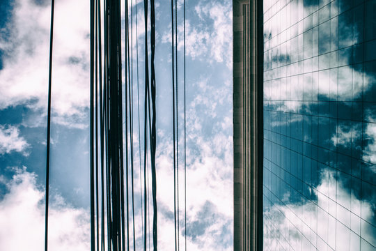 Corporate building facede made of glass windows reflecting clouds with energy wires passing in front of it.