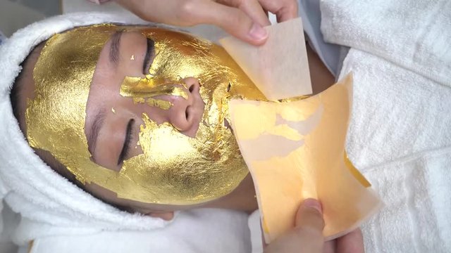 Young woman getting 24 karat gold facial treatment at the beaty clinic. The treatment of using real gold for youthful skin