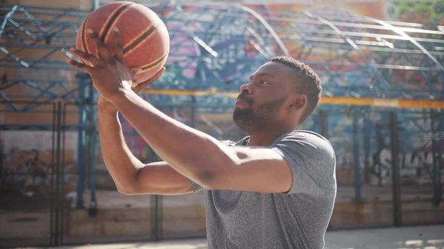 Handsome African guy throwing a basketball to hoop on background of beautiful graffiti. Portrait of attractive young man in gray T-shirt. Outdoors.