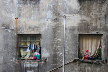 Square windows of homes with clothes and flowers in a decayed building with cracked walls. No...