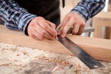 Close-up The man measures a wooden board with a ruler and marks with pencil the necessary points for slices