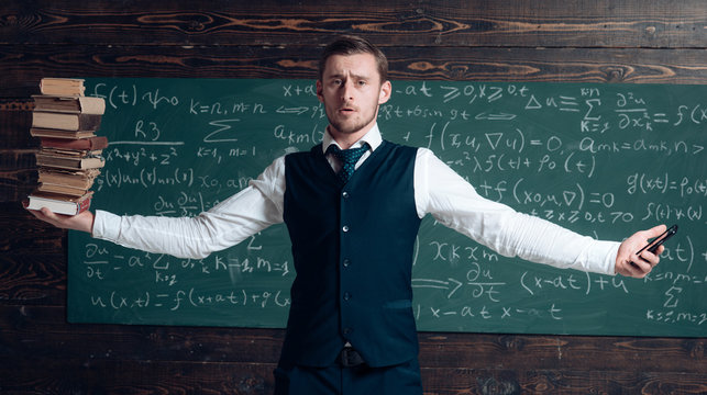 Man teacher balancing in hands pile of books and smartphone as symbol analog and digital information storages. Teacher formal wear, chalkboard background. Balance concept. Modern against outdated