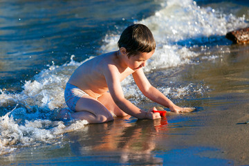 Little joyful happy boy playing and having fun on the beach, smeared with sand.Child Family Concept