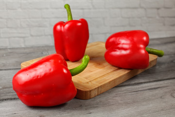 Three whole red bell peppers with drops of water, on chopping board and wooden table.
