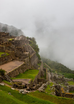 Vertical image of Machu Picchu stone ruins with low clouds on the nature on the background. Peru. South America. No people.