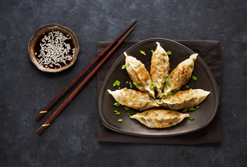 Fried dumplings Gyoza in plate, soy sauce, and chopsticks on a black concrete background, top view
