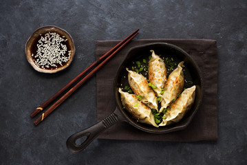 Fried dumplings Gyoza in a frying pan, soy sauce, and chopsticks on a black concrete background, top view