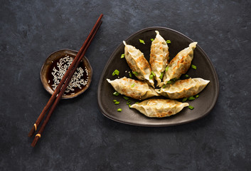 Fried dumplings Gyoza on a plate, soy sauce, and chopsticks on a black concrete background, top view
