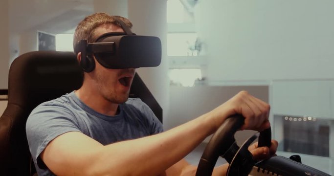 Computer simulation. Cheerful young gamer in virtual reality goggles is expressing excitement while enjoying car racing video game with steering wheel