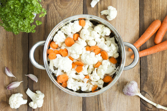 Fresh cauliflower and carrots in a pot. Ingredients to prepare the soup on old wooden table.