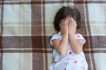 The child is covering the eyes with hands. The view from above.