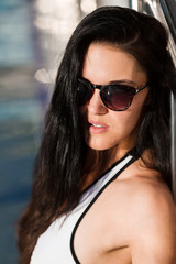 potrait of an attractive young slim brunette woman wearing white swim suit is leaning on the metal fence of a swimming pool. concept of luxury vacation