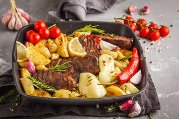 Beef steaks grilled with baked potatoes and vegetables in a pan grill.