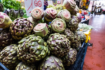 City market stall with red floor with fresh artichokes and price tag. Rome. Europe. No people.