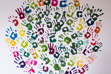 Vertical image of red, yellow, blue, purple, orange and black handprints on a white concrete wall. No people.