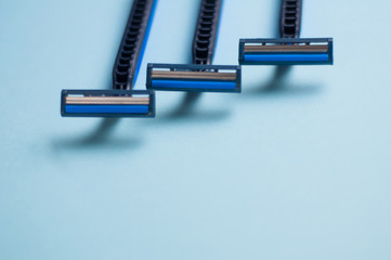 Row of disposable blue and black plastic razors with two blades and one humidifying strip on blue background with copy space