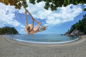 woman in bikini playing in relax sitting on wooden swing under plam tree at sunny on the island, summer time vacation and weekend relax funny happy time