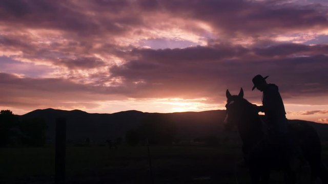 The silhouette of a cowboy against a mountainous backdrop as the sun is setting.