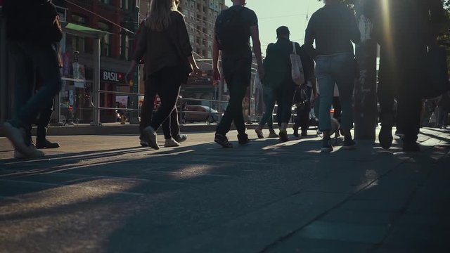 Pedestrians walk along a sidewalk in the evening sun in a low angle slow motion shot
