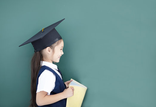side view of little girl in graduation cap and studying