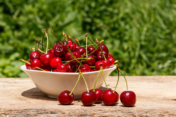 Bowl with fresh cherry on rustic wooden table outdoor
