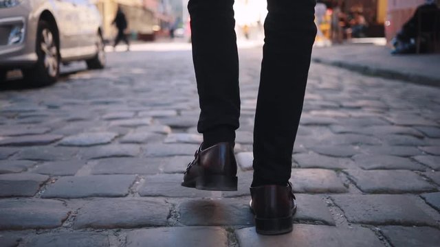 Young brown-haired tall Caucasian man walking on the beautiful street of home town. Guy in business clothes. Springtime. Outdoors.