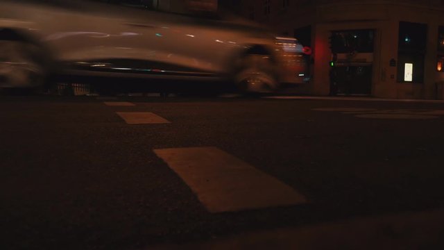 Cars passing by a green light and man crossing the street wearing a suit by night in Paris 4K