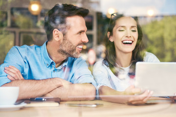 Couple sitting together in cafe looking at tablet and laughing