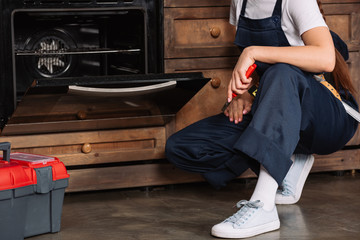 cropped shot of repairwoman with pliers sitting near oven