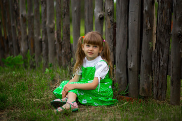 Little girl sitting on green grass in garden in sunny summer day