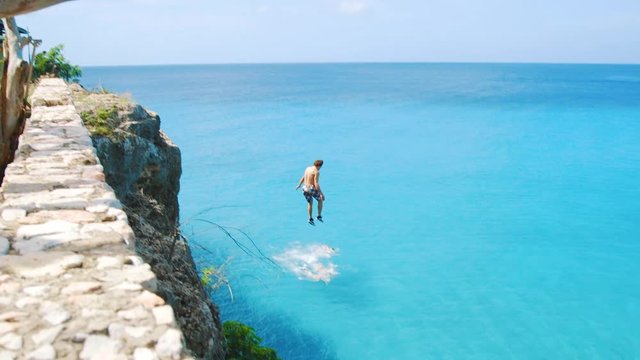 Young person is running and jumping off the high cliff at Playa Forti into turquoise water of Caribbean sea. This cinematic shot is perfect for topics like: adventure time, extreme sports