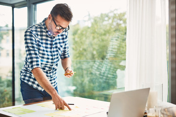 Mid adult man, designer working by desk standing with notes