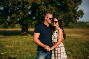 Handsome guy and an attractive girl hug each other near a large green tree. Love story